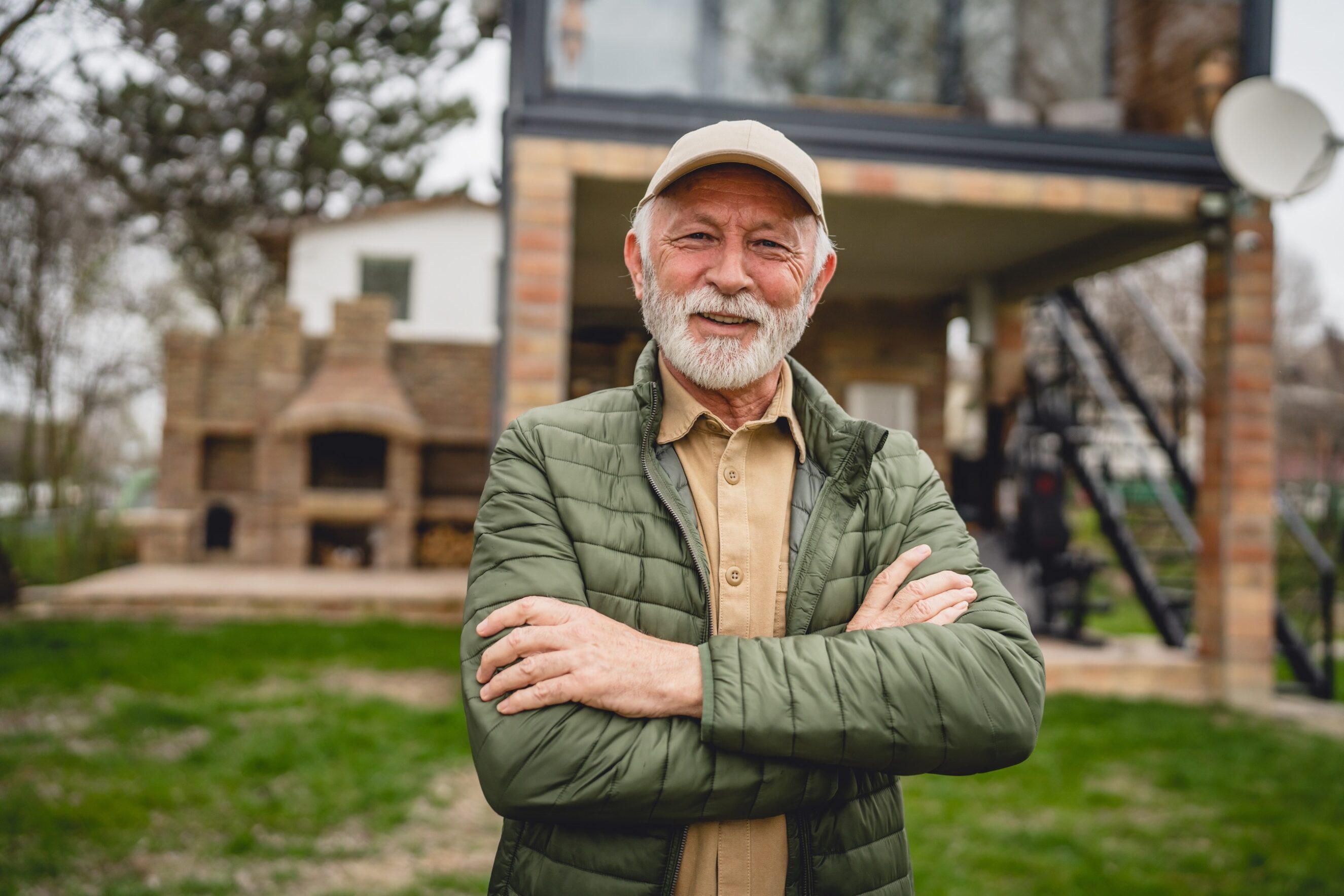 Male grandfather with beard and hat cap stand in front of his house